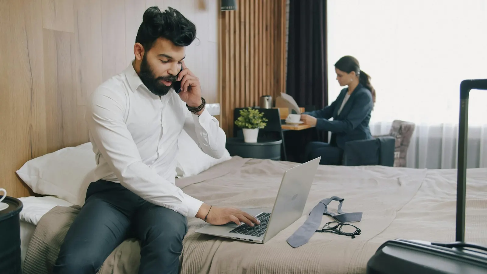 A man on a phone call working on a laptop in a hotel room