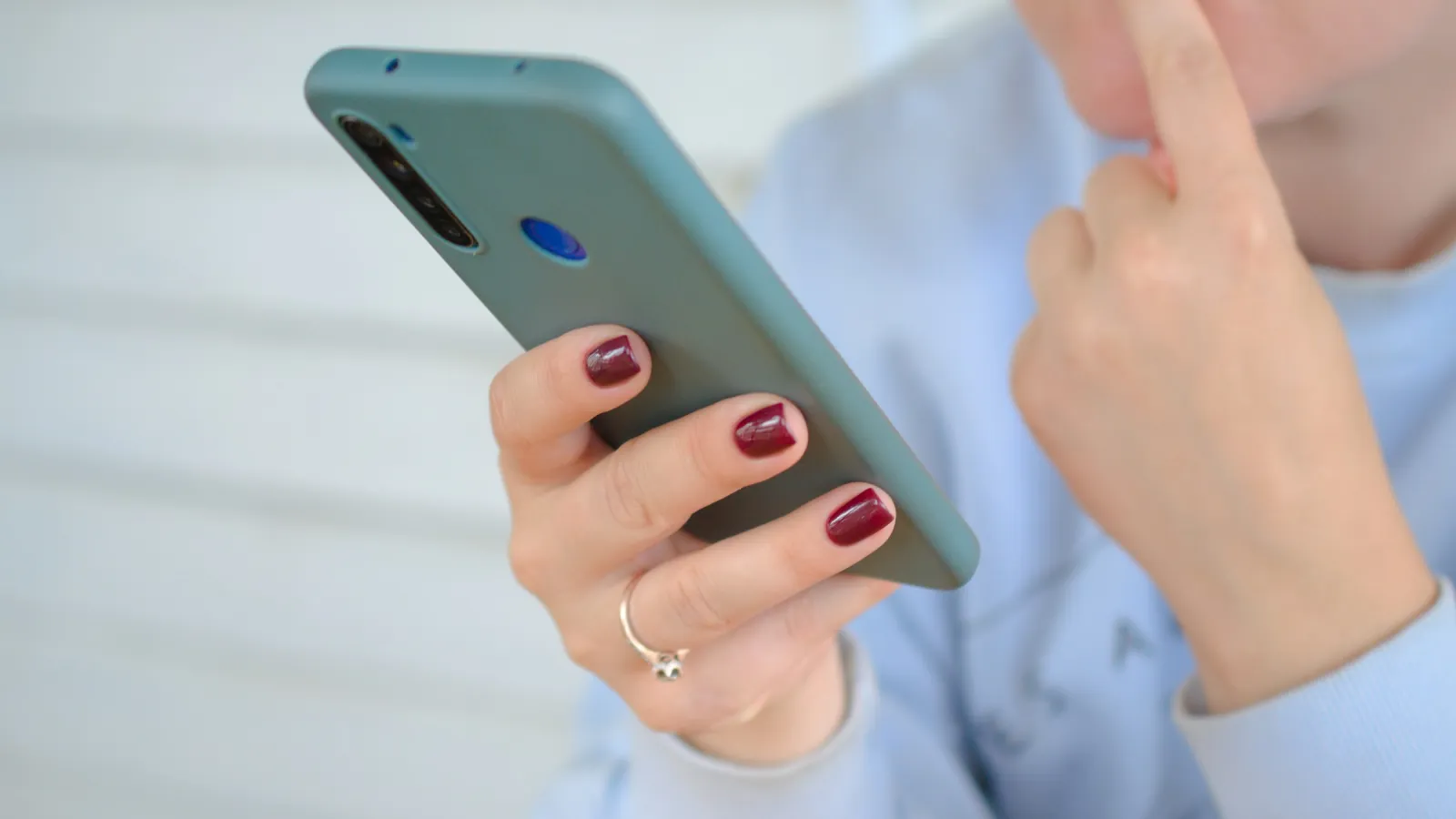 A person in a light blue shirt holding a smartphone and touching their face