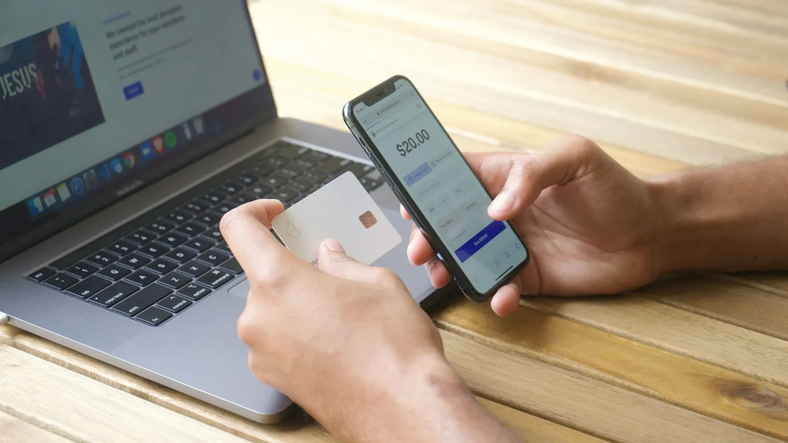 A person paying on a smartphone with a card next to a laptop