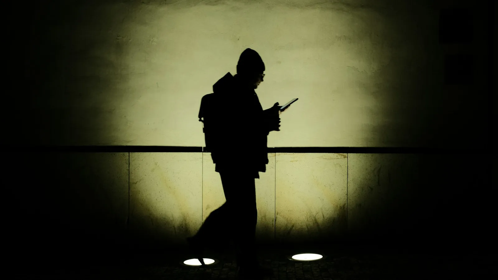 Silhouette of a person walking at night, looking at a phone