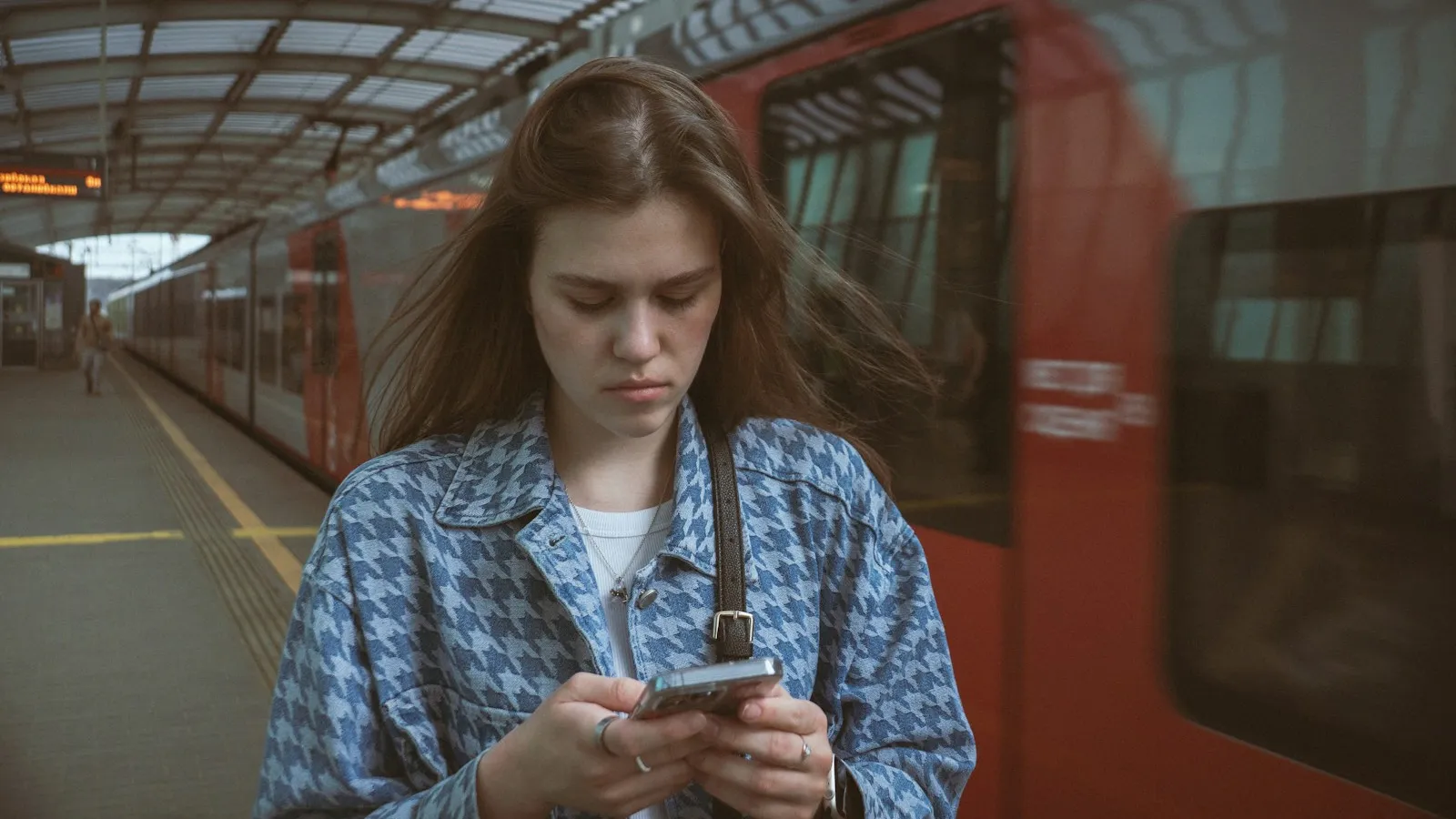 A young woman looking at her phone on a train platform as a train passes