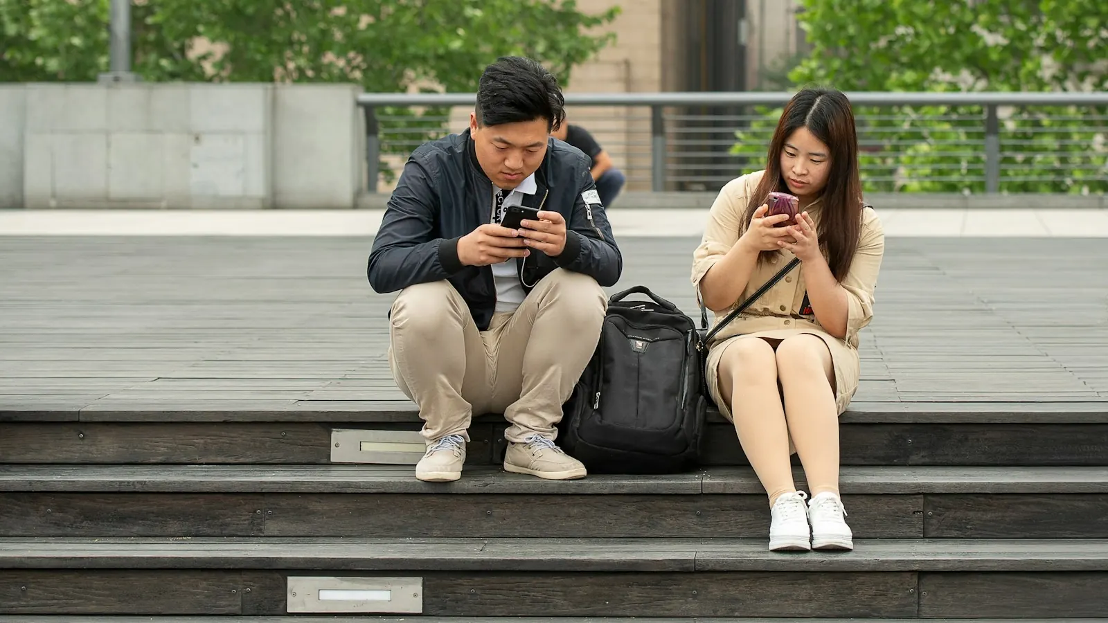 Two people sitting on outdoor steps, each looking at their smartphone