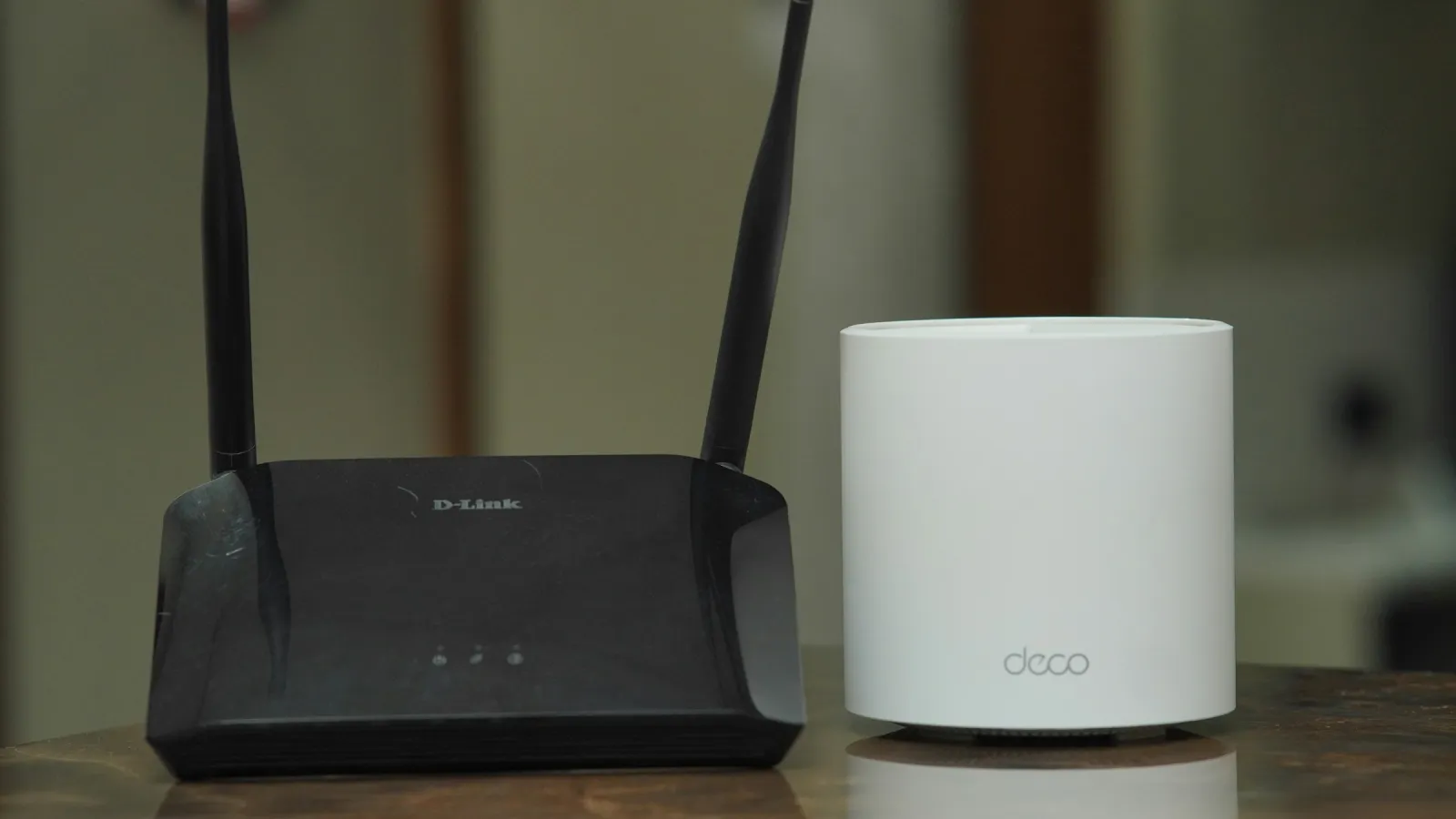 Un router wifi negro con dos antenas junto a un dispositivo mesh blanco sobre una mesa de madera
